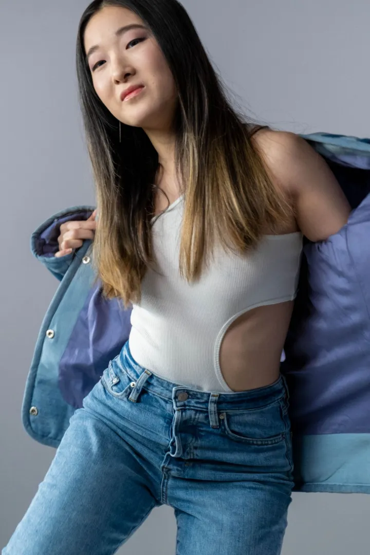 Model memakai kaus rib putih dan jeans, jaket tambal dibuka memperlihatkan lapisan dalam berwarna lembayung