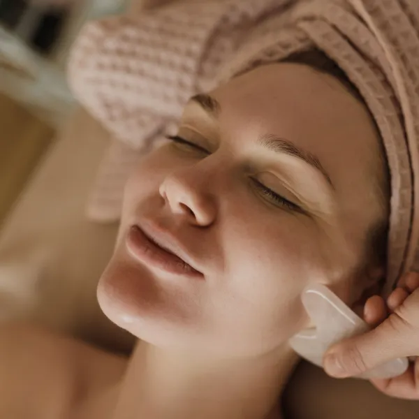 Pelanggan tersenyum dengan mata terpejam saat wajahnya dipijat dengan gua sha